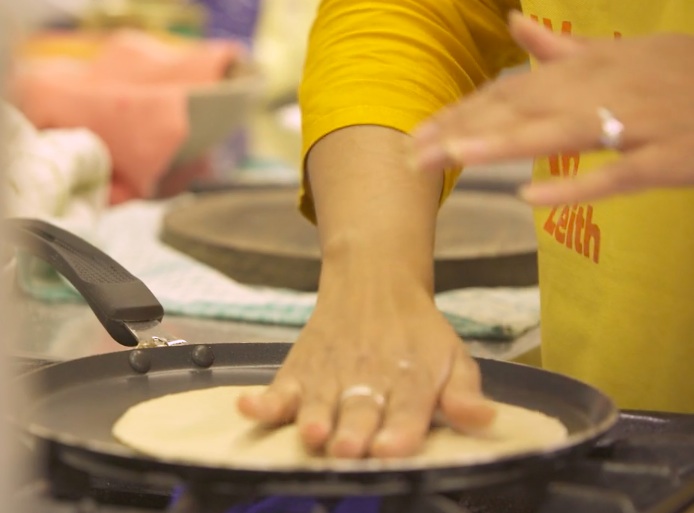close up of Meena's hands skilfully placing chapatis on hot griddle. Image credit http://rarebirdmedia.com/